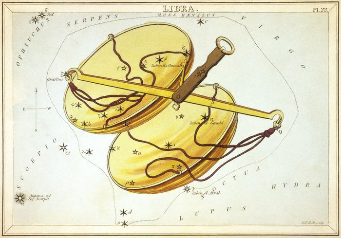 Eine goldene Balkenwaage mit zwei Waagschalen auf einer historischen Sternbildkarte